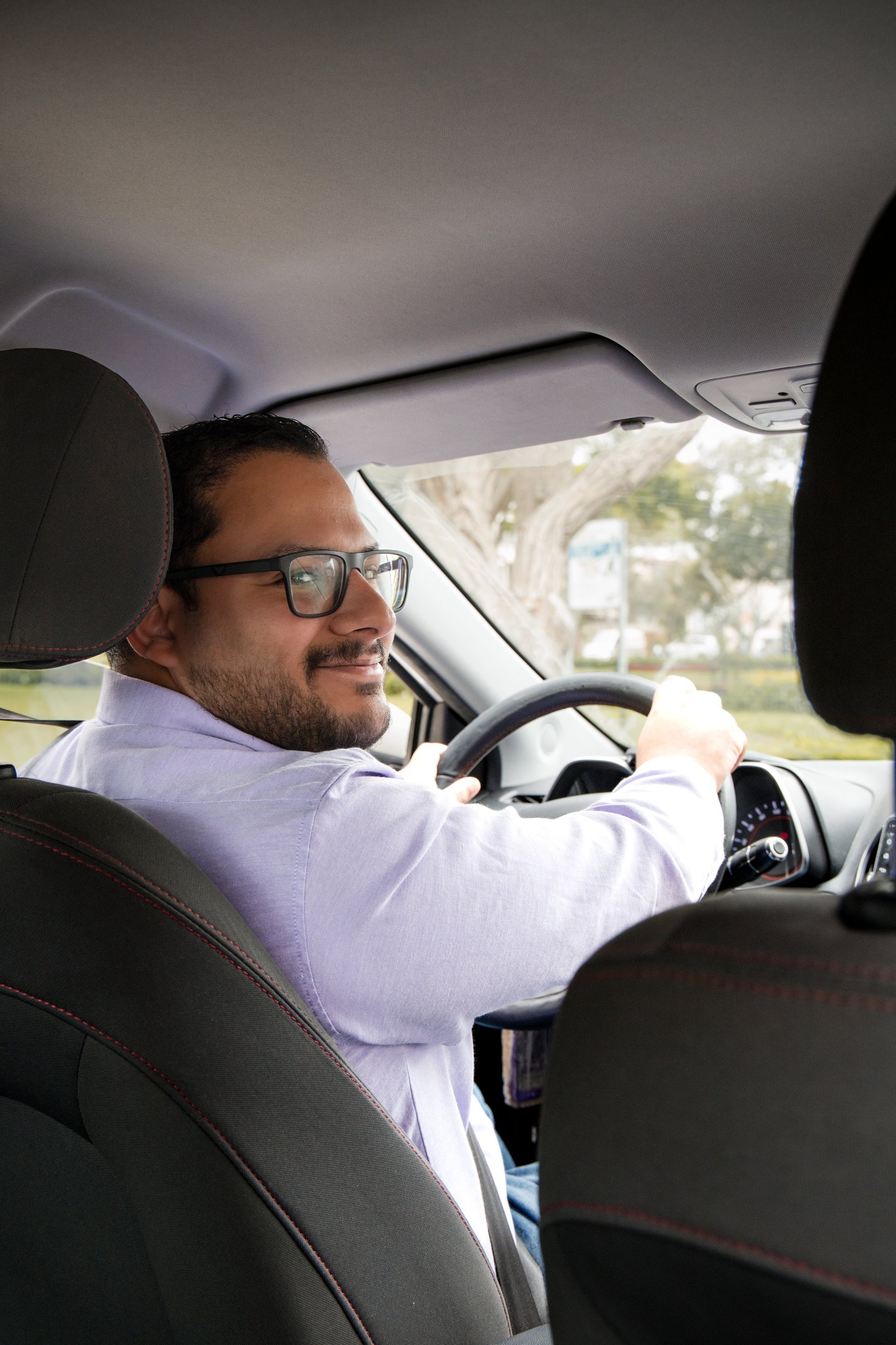 A man in glasses is driving a car smiling